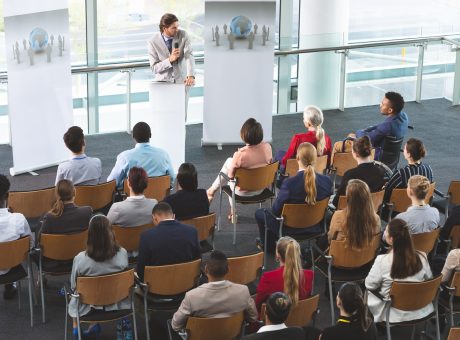 Businessman with microphone speaking in front of business people at business seminar in office